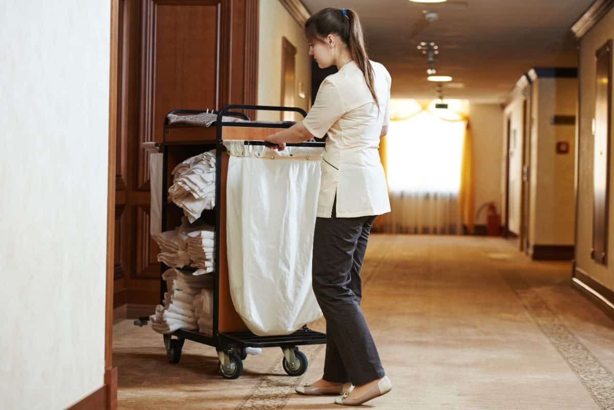 A hotel staff is pushing a cleaning cart in the hallway.