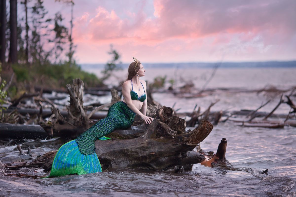 A woman in a mermaid costume on a shore.