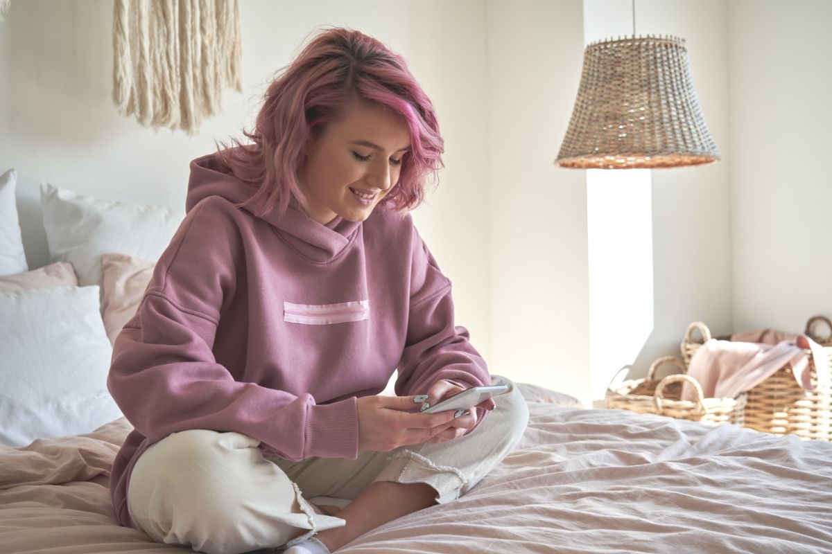 A young woman sitting on the bed and using her phone.