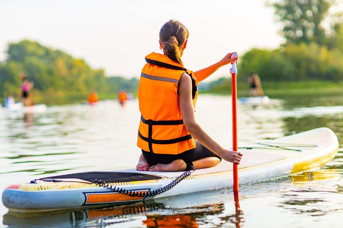 A woman with a life jacket paddling on a surf.