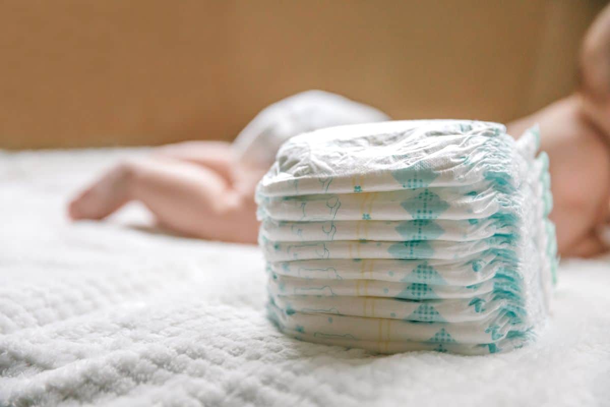 A stack of diapers near a baby.