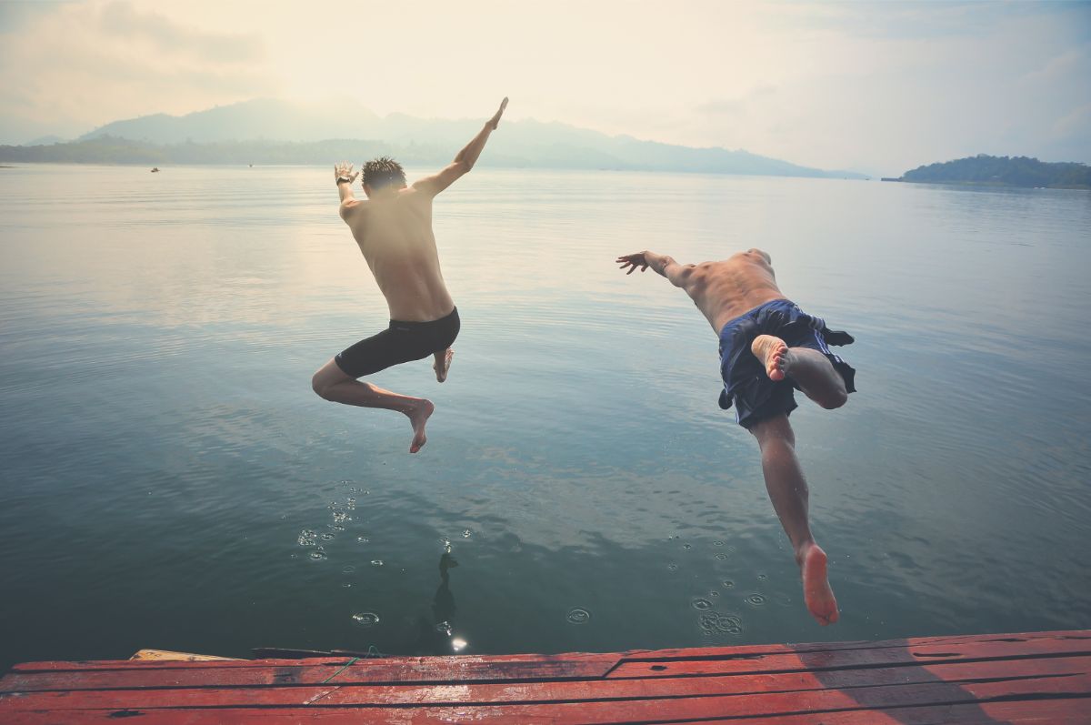 Two guys jumping in a lake.