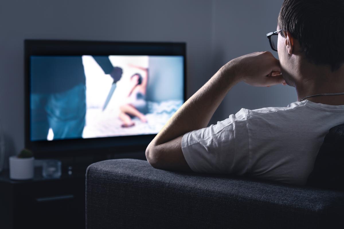 A man watching a horror movie on a TV.